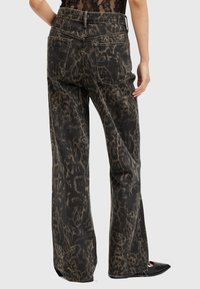 Jeans de estampado de leopardo en negro y marrón, con cintura alta, patas anchas, dobladillo desgastado y dos bolsillos traseros. La tela tiene una textura suave.