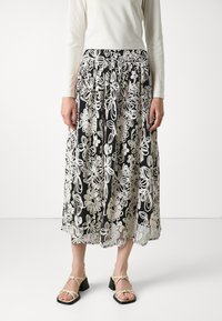 Svart blomstret skjørt med hvit broderi, flytende stoff, plissert design og mid-lengde; brukt med beige sandaler med stropper.
