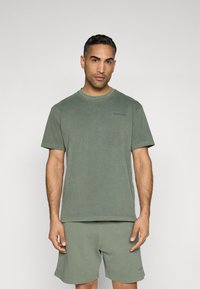 Green cotton t-shirt with short sleeves and a crew neck, featuring a subtle logo on the left chest. Soft texture, paired with matching shorts.
