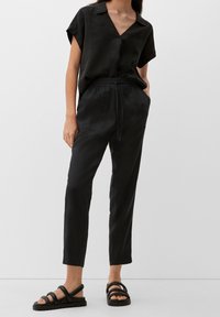 Svart linne skjorta med v-hals och korta ärmar, i kombination med svarta byxor med elastisk midja, sidosfickor och en subtil struktur. Svarta sandaletter med remmar.