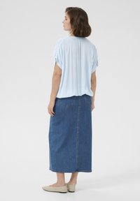 Haut bleu ciel à manches courtes avec une coupe ample, associé à une jupe en jean longue de couleur bleu foncé. Des chaussures plates beiges complètent la tenue.