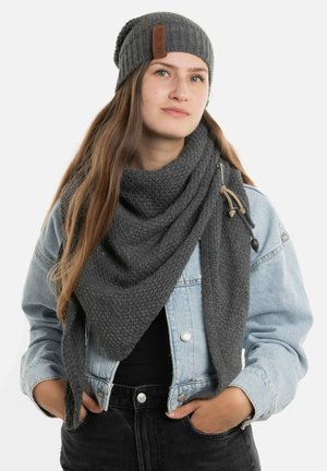 Grijze gebreide beanie met een leren label, gecombineerd met een bijpassende textuursjaal. Draagt een lichte denimjas en zwarte jeans.