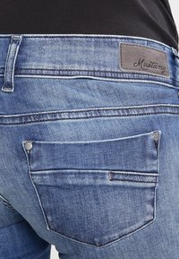 Modré džíny z denimu mají rovný střih, kontrastní švy a logo nášivku na pase, s dvěma zadními kapsami a detaily s nýty.