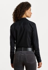 Černá dlouhá košile s límečkem, hladký materiál a manžety na knoflíky, doplněná šedými kordovými kalhotami s zadními kapsami.