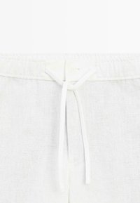Pantalon en lin blanc avec taille élastique et cordon blanc noué en un nœud à l'avant centre.