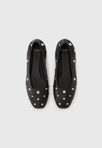 Zapatos planos de cuero negro con punta redondeada, con tachuelas metálicas plateadas distribuidas uniformemente sobre la parte superior. Textura suave, diseño minimalista.