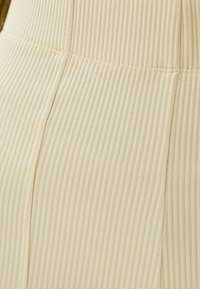 Tejido beige acanalado con líneas verticales, que presenta una textura sutil y detalles de costura a lo largo de las costuras, creando una apariencia ajustada.