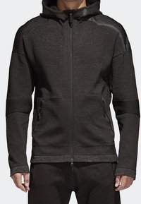 Svart zip-up huvtröja med strukturerad textil, huva och sidofickor. Har ribbade ärmslut och axeldetaljer. Sömlös design och åtsittande form.