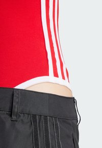 Röd bodysuit med vita ränder tillsammans med svarta shorts med en slät yta och dragsko i midjan, med vertikala plisseringar nertill.