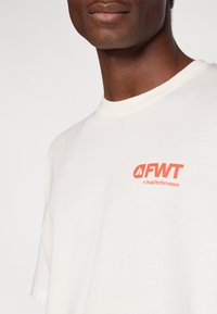 Λευκό βαμβακερό μπλουζάκι με πορτοκαλί λογότυπο "FWT by PeakPerformance" στην αριστερή πλευρά �του στήθους, κοντά μανίκια και ριμπ τελείωμα στον λαιμό.