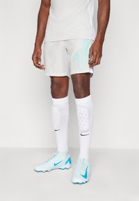 Lyse grå treningshorts med en turkis Nike-logo, sammen med hvite sokker og lyseblå fotballsko med sporty design og grep.