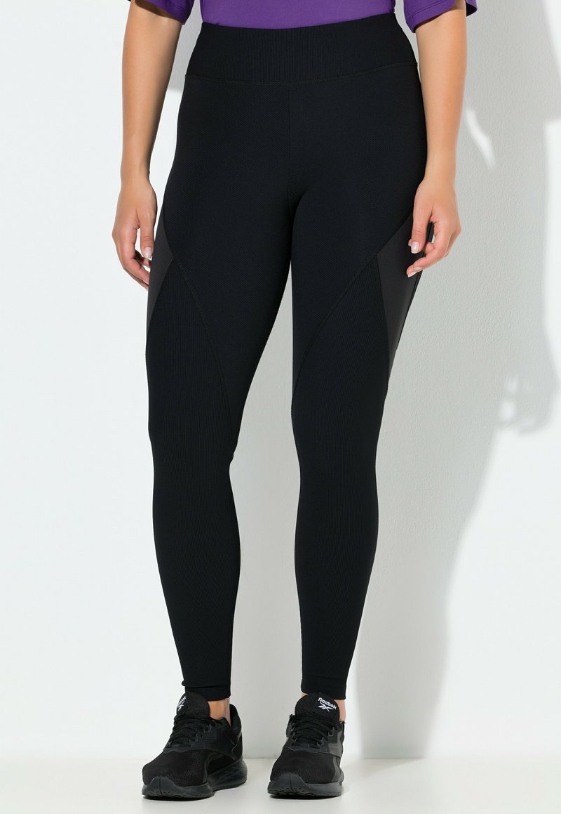 Czarne legginsy o prążkowanej fakturze, z wysokim pasem i kontrastowymi panelami bocznymi. Połączone z czarnymi butami sportowymi.