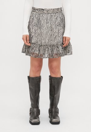 Frau trägt einen schwarz-weiß gestreiften Zebra-Muster Rock mit Volant- Saum, weißes langärmeliges Oberteil und schwarze knielange Lederstiefel.