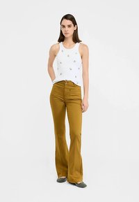 Débardeur blanc sans manches avec broderie florale, assorti à un pantalon évasé moutarde. La tenue présente des textures lisses et une coupe ajustée.