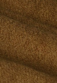 Gros plan sur un tissu brun doux et bouclé avec une surface texturée semblable à de la laine et de fins détails dans des tons terreux chauds.