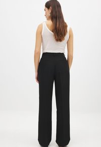 Pantalones negros ajustados con una cintura alta, pliegues delanteros y dos bolsillos traseros, combinados con una camiseta sin mangas clara. Tela suave y pierna recta.