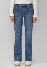 Helleblaue Denim-Jeans mit geradem Bein, ausgestattet mit zwei Fronttaschen, kontrastierenden Nähten und einem umgeschlagenen Saum. Kombiniert mit weißen Sneakers.
