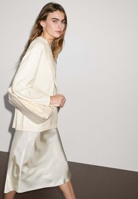 Maglione in maglia crema, gonna a sottoveste in satin beige chiaro e borsa a tracolla beige; texture morbide e design minimal.