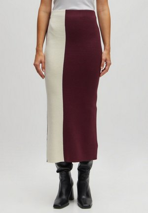 Gebreide midi rok met een bordeauxrode en crèmekleurige kleurblokontwerp; gladde textuur; aangesloten silhouet; zijsplitdetails. Gecombineerd met zwarte laarzen.