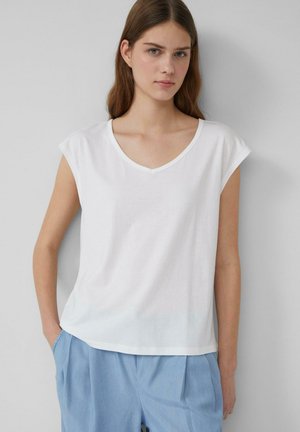 Witte katoenen t-shirt met een V-hals en korte mouwen, met een ontspannen pasvorm en een gladde textuur. Draagt met lichtblauwe broeken.