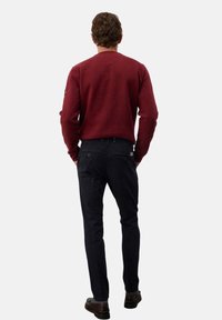 Felpa bordeaux con polsini e fondo a coste, abbinata a jeans scuri. L'outfit presenta un taglio slim e una sottile grafica sul denim.