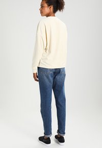 Crewneck sweatshirt i myk kremfarge kombinert med avslappede blå jeans. Antrekket har oppbrettede mansjetter og svarte sneakers.