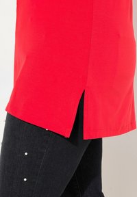 Rode tuniek met zijsplitten, gemaakt van een soepele stof. Gecombineerd met donkere jeans met parelaccenten. Strak ontwerp met een moderne pasvorm.
