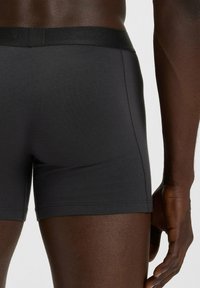 Boxer in cotone nero con una texture liscia, dotati di una cintura elastica abbinata e una vestibilità aderente, mostrati da un angolo laterale.