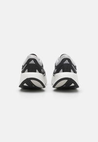 Chaussures de sport noires et grises avec une tige en maille texturée et une semelle blanche rembourrée. Présente des accents latéraux obliques et un logo de marque près du talon.