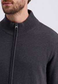 Dunkelgrauer Reißverschluss-Pullover mit geripptem Kragen und glatter Textur. Verfügt über einen kurzen Reißverschluss und eine taillierte Passform. Keine sichtbaren Muster oder Akzente.