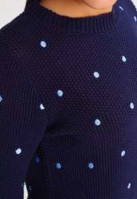 Marinblå stickad tröja med rund hals, prydd med ljusblå broderade prickar jämnt fördelade över tygstrukturen.