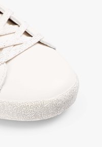 Witte leren sneaker met een gestructureerde rubberen zool, met contrasterende lichte veters en een glad ronde neus. Subtiel reliëfpatroon op de zool.