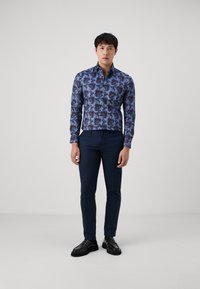 Blus med långa ärmar i blått med blommönster, i kombination med mörkblå slim fit-byxor och svarta skor. Slät textur och strukturerad design.