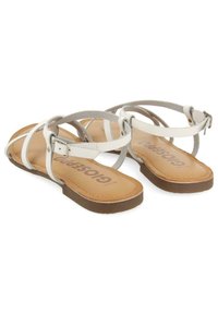 Sandali strappy bianchi e grigi con suola piatta, caratterizzati da una parte superiore in tessuto morbido e una soletta marrone con texture. Inclusa una fascia alla caviglia regolabile.