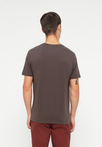 Camiseta de algodón marrón con cuello redondo y mangas cortas, que presenta una textura suave y un diseño ligeramente ajustado.