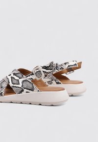 Sandales à imprimé serpent noir et blanc, avec des brides croisées et une boucle, reposant sur une semelle plateforme blanche avec un détail texturé.
