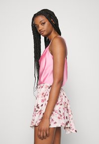 Top de cetim rosa com alças finas, combinado com uma saia mini de estampado floral com flores rosa e bege sobre um fundo claro.