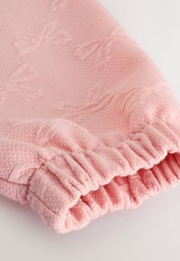 Tessuto rosa strutturato con polsino a coste, caratterizzato da un delicato motivo floreale. Materiale morbido e tessuto con dettaglio arricciato alla fine.