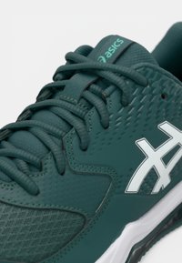 Teal treningsko med tekstureret syntetisk overdel, forsterket tå og kontrastfarget hvit logo. Har flate lisser og polstret krage for komfort.