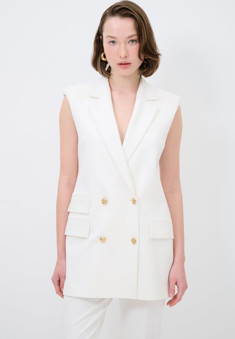 Bílý tailored vest s hlubokým V výstřihem, dvoucestným designem, zlatými knoflíkovými akcenty a bočními kapsami; hladká tkanina, bez rukávů.