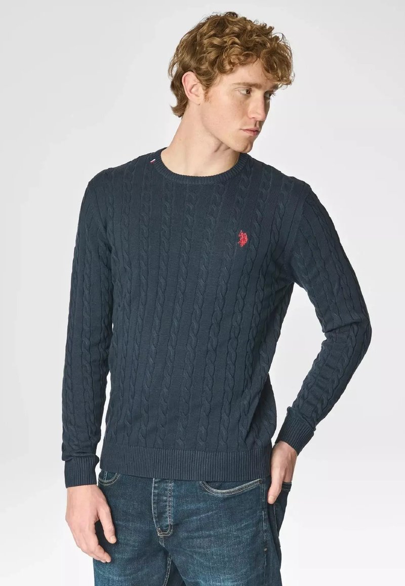 Maglione lavorato a maglia blu navy, design a treccia, scollo rotondo, polsini e orlo a coste. Piccolo logo rosso decorativo sul petto.