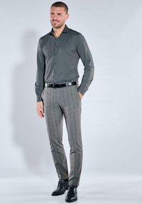 Graues Langarmhemd mit Knöpfen, kombiniert mit grauen karierten Hosen und schwarzen Schuhen. Der Gürtel ist ebenfalls schwarz, und die Passform ist maßgeschneidert.