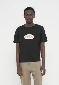 Μαύρο βαμβακερό μπλουζάκι με κόκκινο και λευκό οβάλ λογότυπο με κείμενο. Κοντά μανίκια, στρογγυλή λαιμόκοψη και άνετη γραμμή.