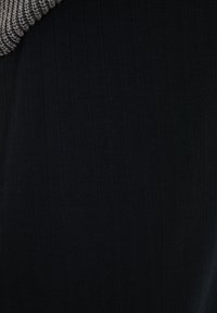 Tejido negro con canalé que presenta una cinta de punto gris texturizada en el escote, creando una apariencia de capas. Diseño elegante y ajustado.