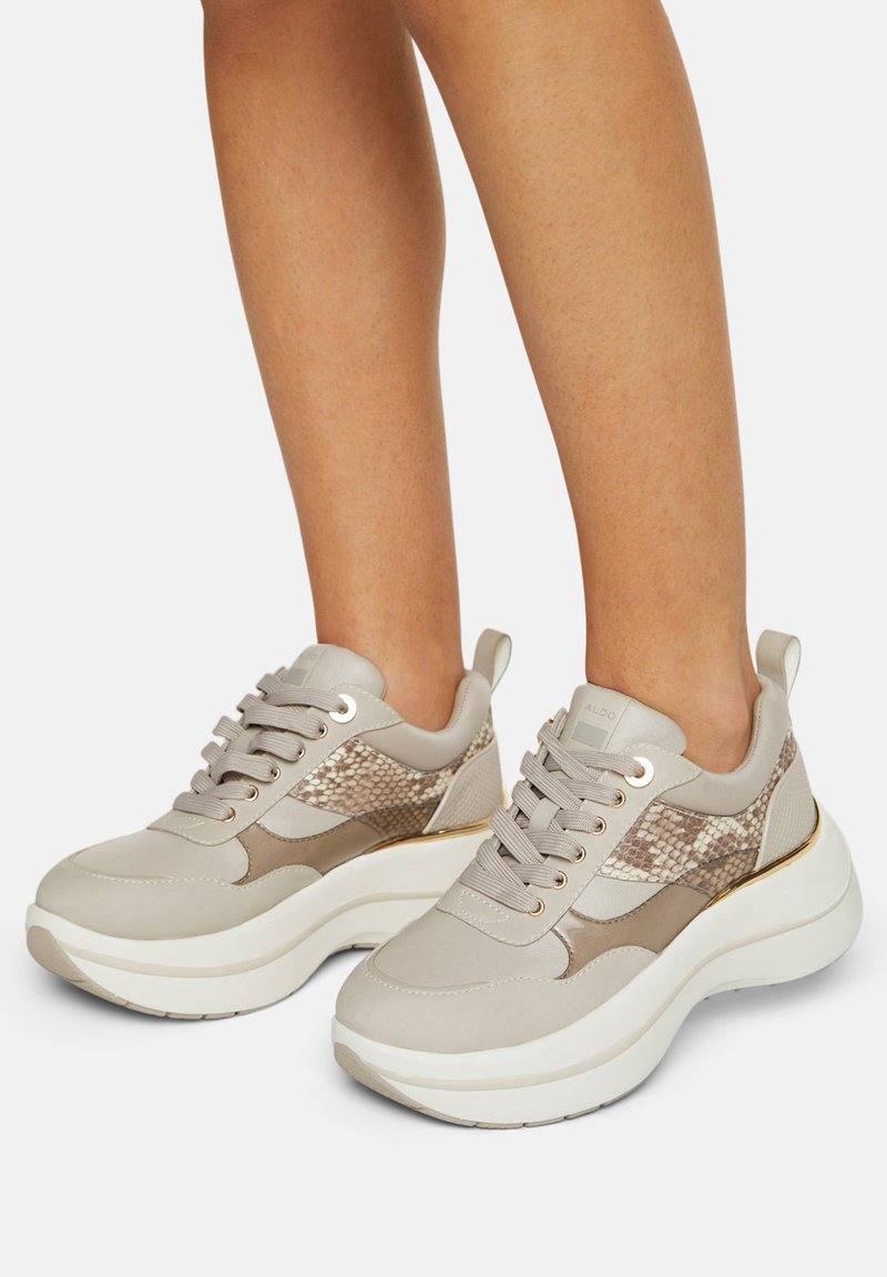 Beige sneakers med en glat læderoverdel, slange-mønstrede detaljer, tyk hvid sål og stofnetpaneler. Synlige detaljer i sølvhardware.