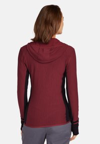Maglietta a maniche lunghe bordeaux con texture a coste, cappuccio e pannelli laterali neri. Include fori per il pollice nei polsini per un maggiore comfort.