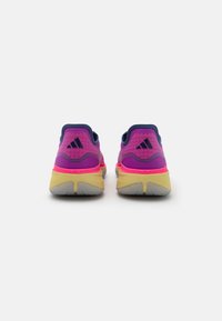 Scarpe da atletica viola e rosa con una tomaia testurizzata, suola imbottita e accenti gialli a contrasto sulla suola.