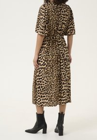 Robe midi en imprimé léopard beige et noir, avec des manches courtes, une taille cintrée et un ourlet fluide. Une paire de bottines noires vient compléter le look.