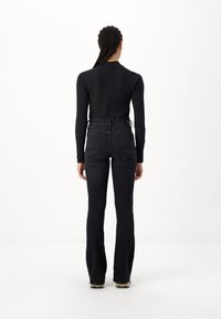 Top negro de manga larga con cuello alto, combinado con jeans acampanados de mezclilla oscura que tienen bolsillos traseros y cintura ajustada.