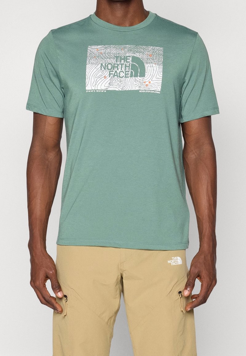 Jasnozielona koszulka z krótkim rękawem, wykonana z miękkiego materiału. Posiada prostokątny nadruk z topograficznym wzorem i logo marki.